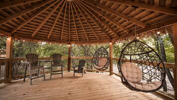 A wooden gazebo with a thatched roof, hanging chairs, and wooden deck.
