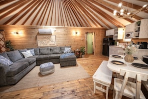 Un ambiente accogliente con soffitto in legno, un divano angolare grigio, un tavolo da pranzo con sedie e un angolo cottura.