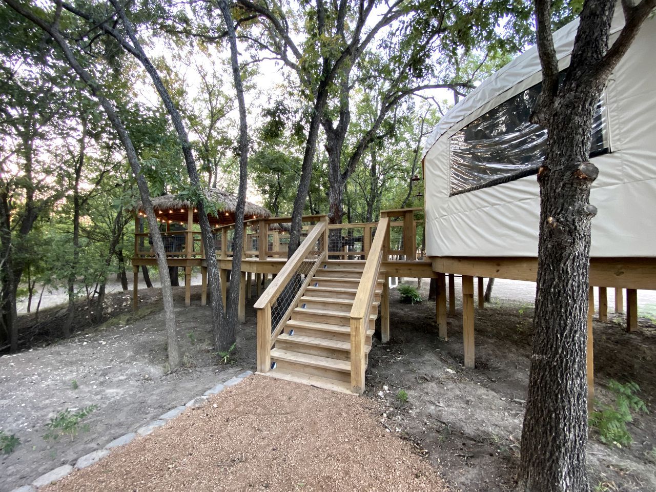 A wooden staircase leading to a treehouse structure, surrounded by trees and a tent-like structure.