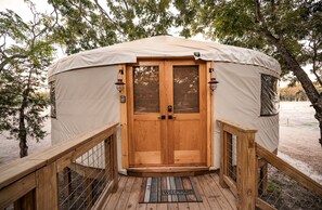 Une tente circulaire avec une porte en bois, une terrasse en bois et un paillasson.