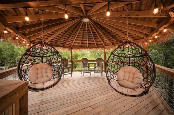 A wooden deck with hanging chairs and a thatched roof.