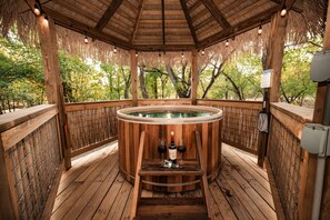 Un bain à remous en bois, avec une terrasse en bois, entouré d’une clôture en bambou et surmonté d’une pergola en bois.