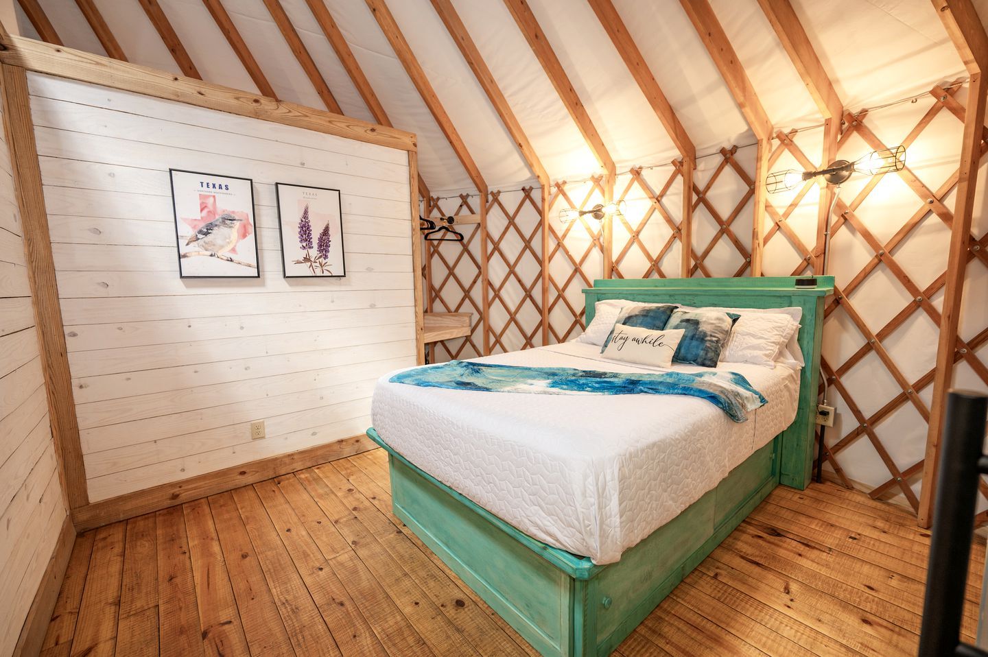 Un dormitorio acogedor con techo de madera, una cama con cabecera verde y dos cuadros en la pared.