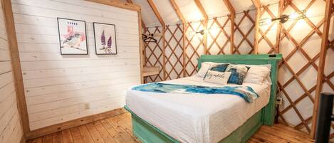 Un dormitorio acogedor con techo de madera, una cama con cabecera verde y dos cuadros en la pared.