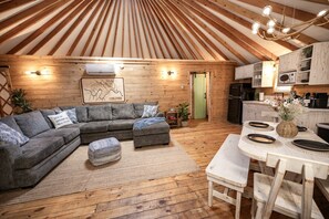 Un intérieur chaleureux avec un plafond en bois, un canapé d’angle gris, une table à manger avec des chaises et un coin cuisine.