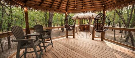 Una terraza de madera con techo de paja, rodeada de árboles.