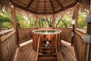 A wooden hot tub with a wooden deck, surrounded by a bamboo fence, and a wooden pergola overhead.