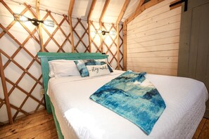 A cozy, wooden-framed room with a bed, a quilt, and a pillow with the text 'stay awhile.'