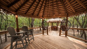 Une terrasse en bois surmontée d’un toit de chaume, entourée d’arbres.