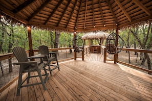 Une terrasse en bois surmontée d’un toit de chaume, entourée d’arbres.