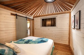 A wooden-paneled room with a bed, a window, and a door.