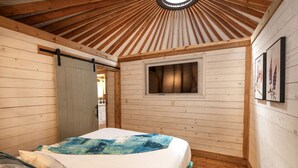 Une pièce aux murs lambrissés, avec un lit, une fenêtre et une porte.
