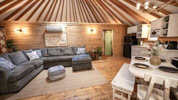 A cozy interior with a wooden ceiling, a grey sectional sofa, a dining table with chairs, and a kitchen area.