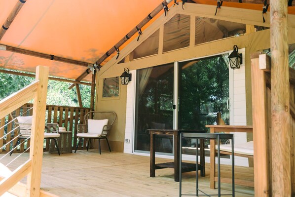 Una terraza de madera con zona de estar cubierta, una escalera y un gran ventanal corredera.