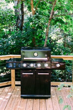 A black grill with four burners on a wooden deck.