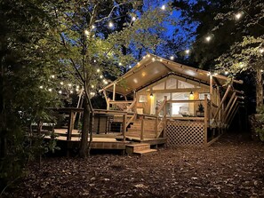 Una cabaña de madera con terraza, rodeada de árboles y luces colgantes.