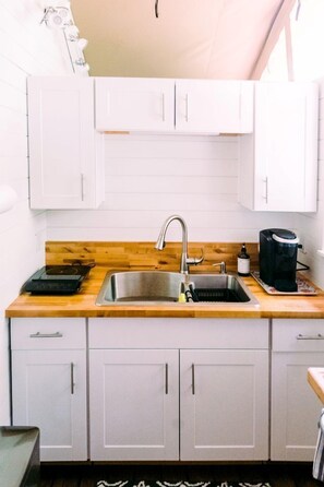 Una cocina con armarios blancos, encimera de madera, pileta de acero inoxidable y cafetera.
