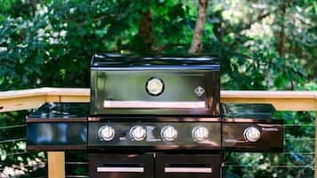 A black grill with four burners on a wooden deck.