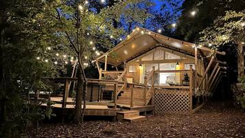 A wooden cabin with a deck, surrounded by trees and string lights.