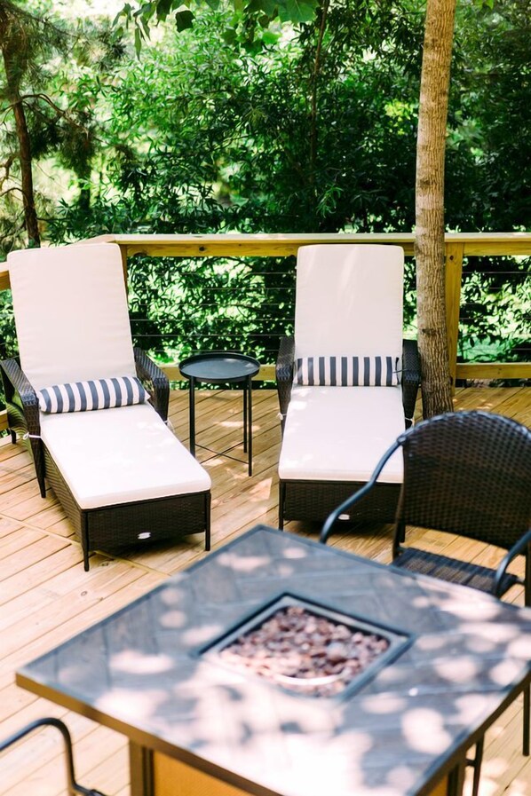 A wooden deck with two lounge chairs and a table with a fire feature.