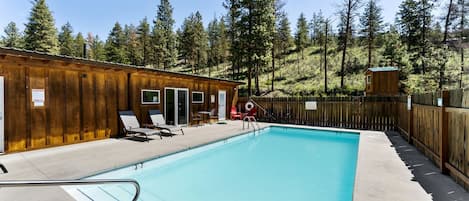 Zona de piscina con cabañas de madera, sillas de descanso y una vista despejada del bosque circundante.