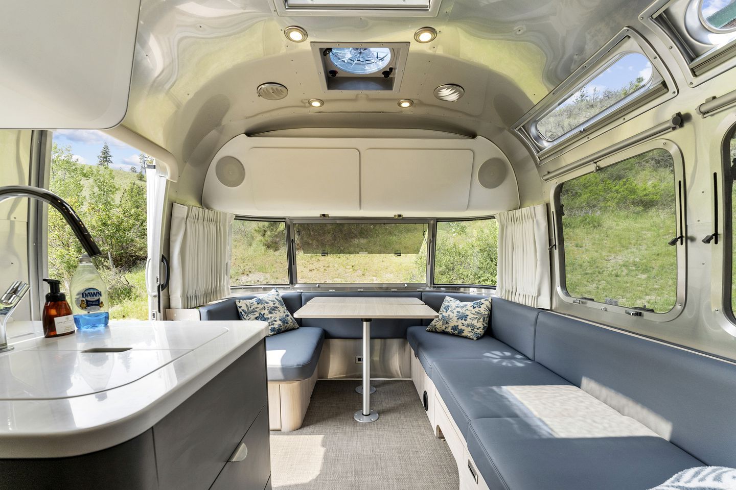 Interior compacto de autocaravana con kitchenette, zona de estar y ventanas amplias.