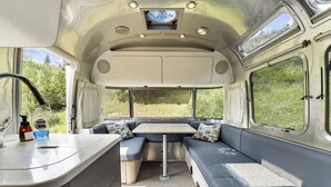 A compact RV interior with a kitchenette, seating area, and large windows.