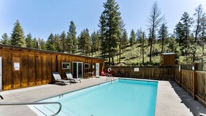 A pool area with wooden cabins, lounge chairs, and a clear view of the surrounding forest.