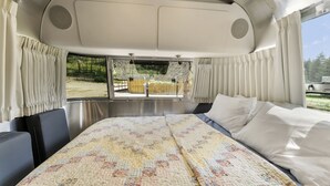 A spacious RV interior with a large bed, a dining area, and a view of the outdoors.