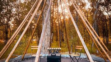 A wooden structure with a bench and a portable grill in a forest.