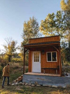 A small wooden cabin with a white door, a window, and a porch with steps leading up to it.