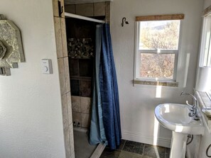 A bathroom with a shower, a window, and a sink.