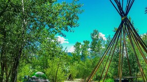 A traditional tipi structure with a circular seating area and a dining table, surrounded by trees and a picnic setup. - Riverside Campsite in Colorado (Paonia)