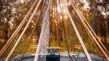 A wooden structure with a bench and a portable grill in a forest.