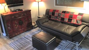 Una sala de estar con un sofá, un televisor, una lámpara y un aparador decorativo.