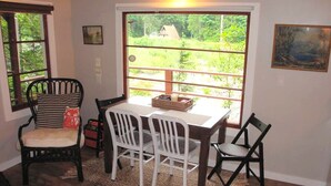Un comedor con una mesa y sillas, una ventana con vistas a la vegetación y un cuadro en la pared.