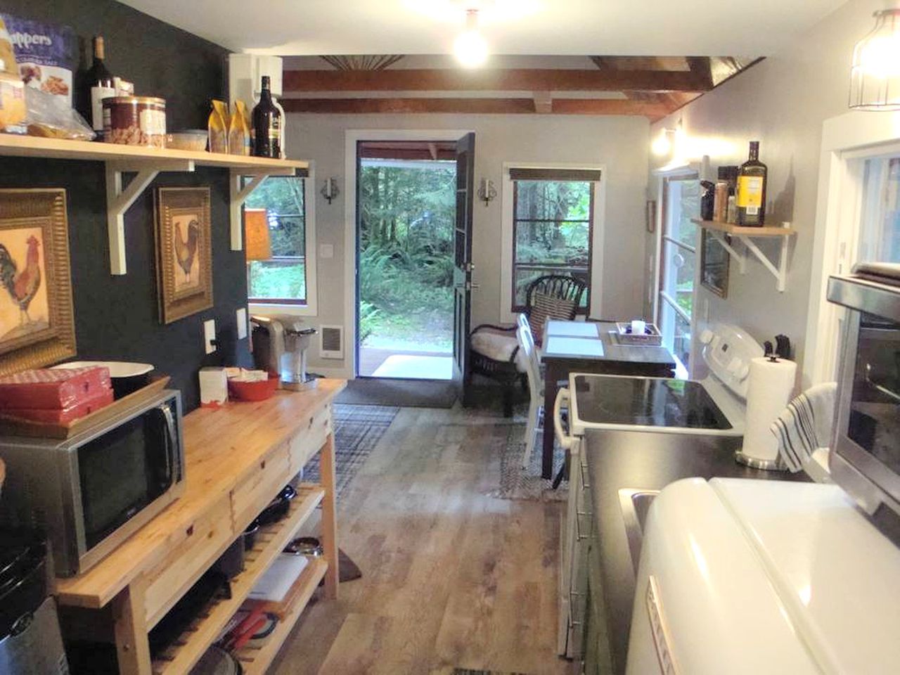 Cocina compacta con microondas, tostadora y refrigerador. Hay un comedor con una silla y una mesa. La habitación tiene piso de madera y un ventanal grande.