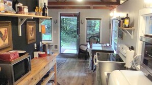Cocina compacta con microondas, tostadora y refrigerador. Hay un comedor con una silla y una mesa. La habitación tiene piso de madera y un ventanal grande.