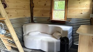 A cozy room with a wooden ceiling, a white sofa, a small window, and a heater. - Cozy Tiny Cabin by the Creek for a Unique Pet-Friendly Getaway in Hillsville, Virginia (Hillsville)