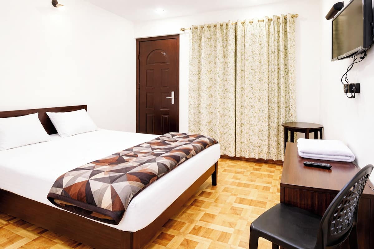 Une chambre d’hôtel avec un lit, un bureau, une chaise, une télévision et une porte.