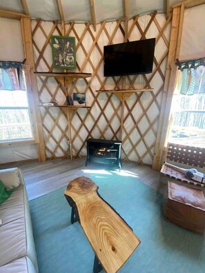 Una habitación acogedora con suelo de madera, un sofá, una mesa baja de madera, una chimenea, un televisor fijado a una pared enrejada y estanterías con diversos objetos.