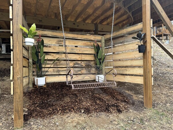 Un columpio de madera con cadenas de metal, rodeado de muros de madera y plantas en macetas.