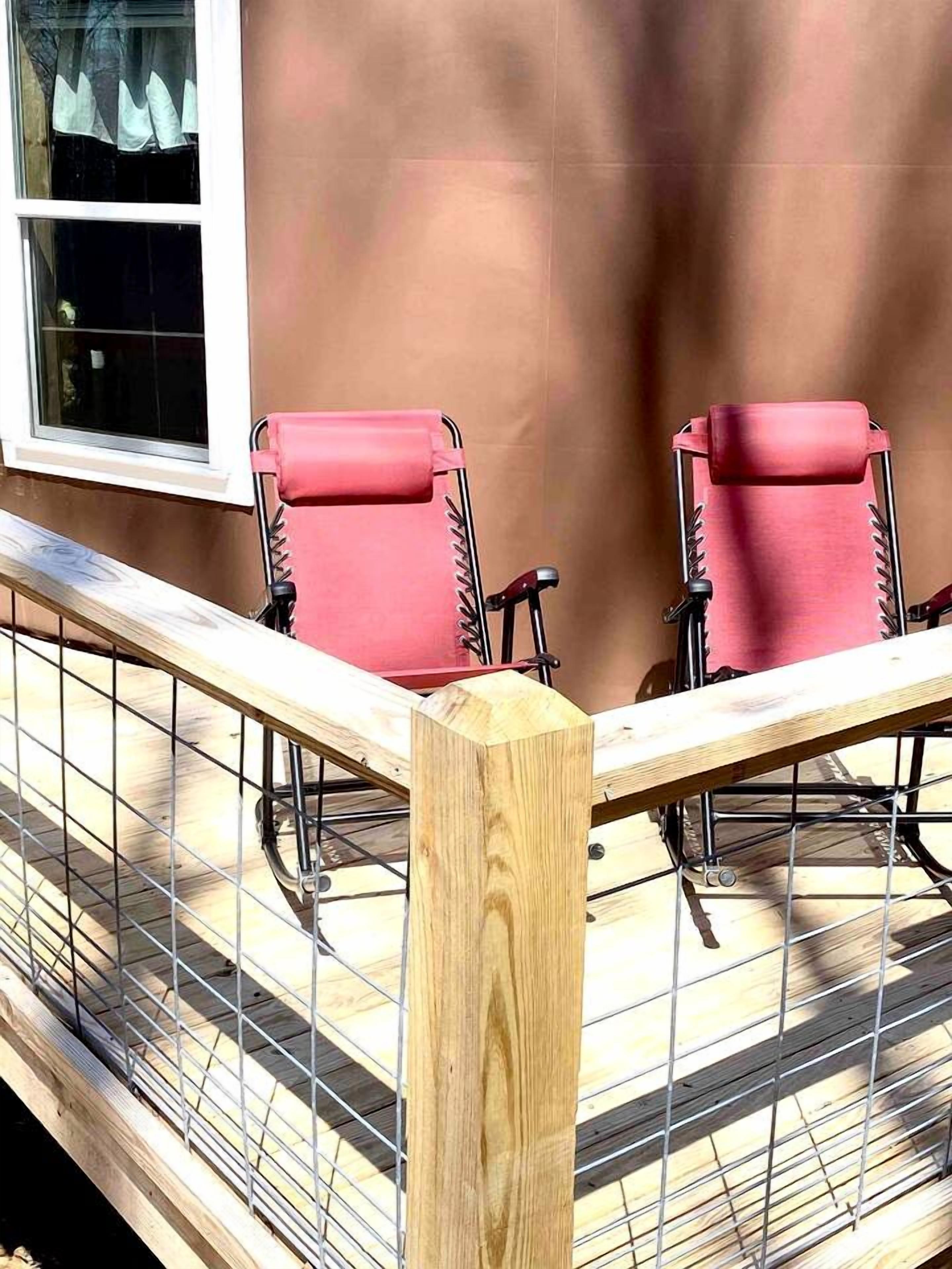 A balcony with two red chairs, a wooden post, and a metal railing.