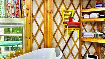 A bathroom with a bathtub, wooden lattice wall, a yellow chair, and shelves with towels and toiletries.