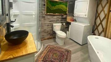 A bathroom with a glass shower enclosure, a wooden vanity, a toilet, a washing machine, and a bathtub.