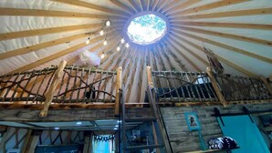 A yurt with a central skylight, wooden beams, and a ladder leading to the upper level.