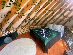Un dormitorio en el ático con una cama, una alfombra blanca y vigas de madera.