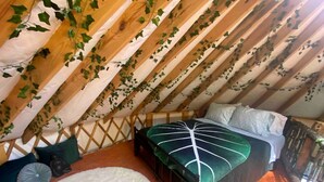 An attic bedroom with a bed, a white rug, and wooden beams.