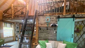 A loft-style room with a wooden ladder, a sofa with green and white cushions, and a turquoise door.