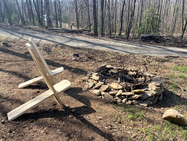 A wooden chair and a stone fire pit in a forested area.